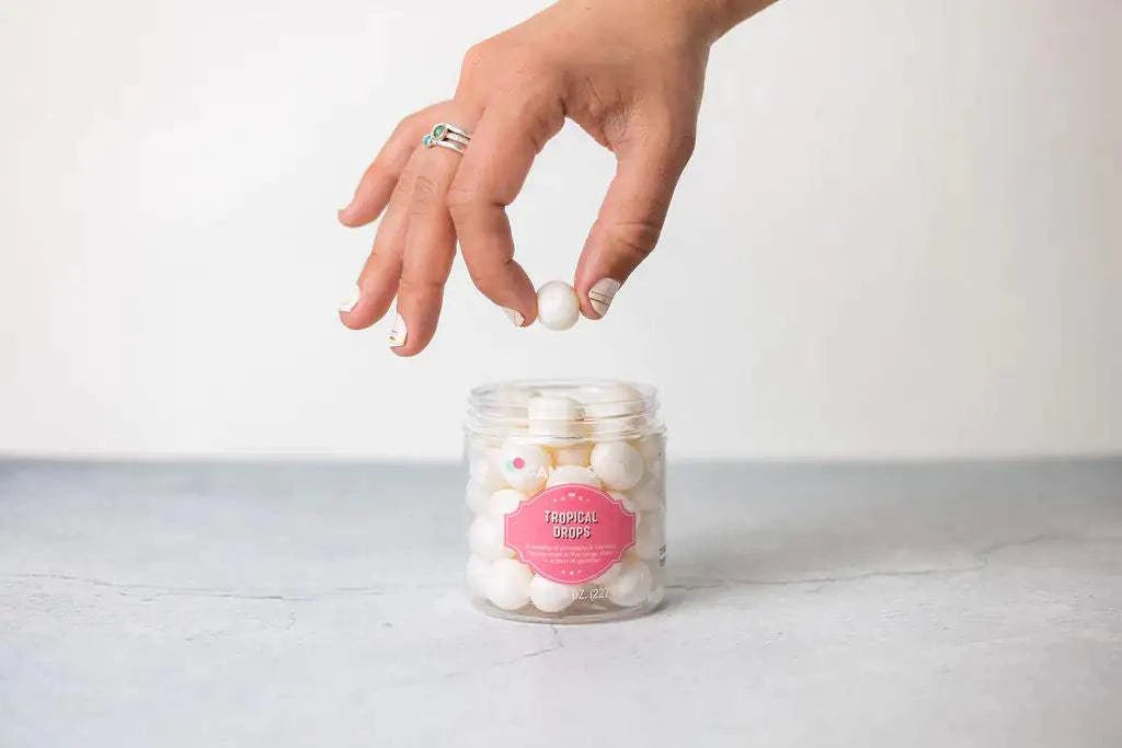 Hand picking white candy from jar labeled "Tropical Drops" for a celebration gift box.
