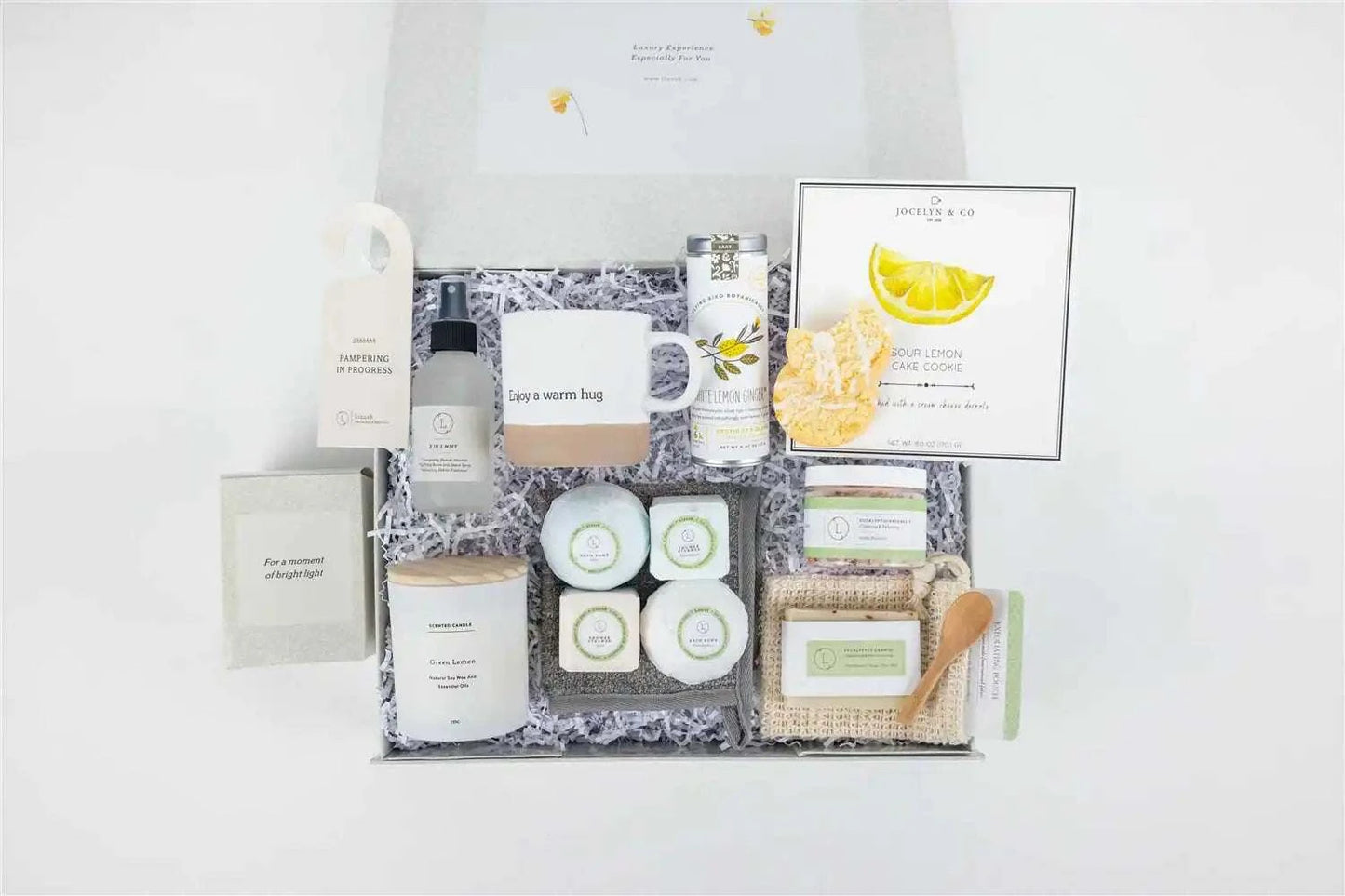 Natural care package gift basket with ceramics, scented candle, shower steamers, bath bombs, eucalyptus soap, salt, tea bags, lemon cookies, soap saver, mist, towel, and personalized options.