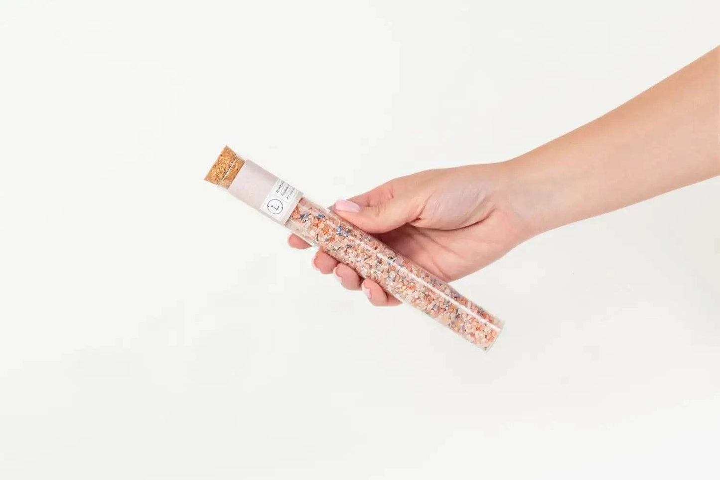 Natural bath salt in a clear glass tube held by a hand, luxurious bath experience.