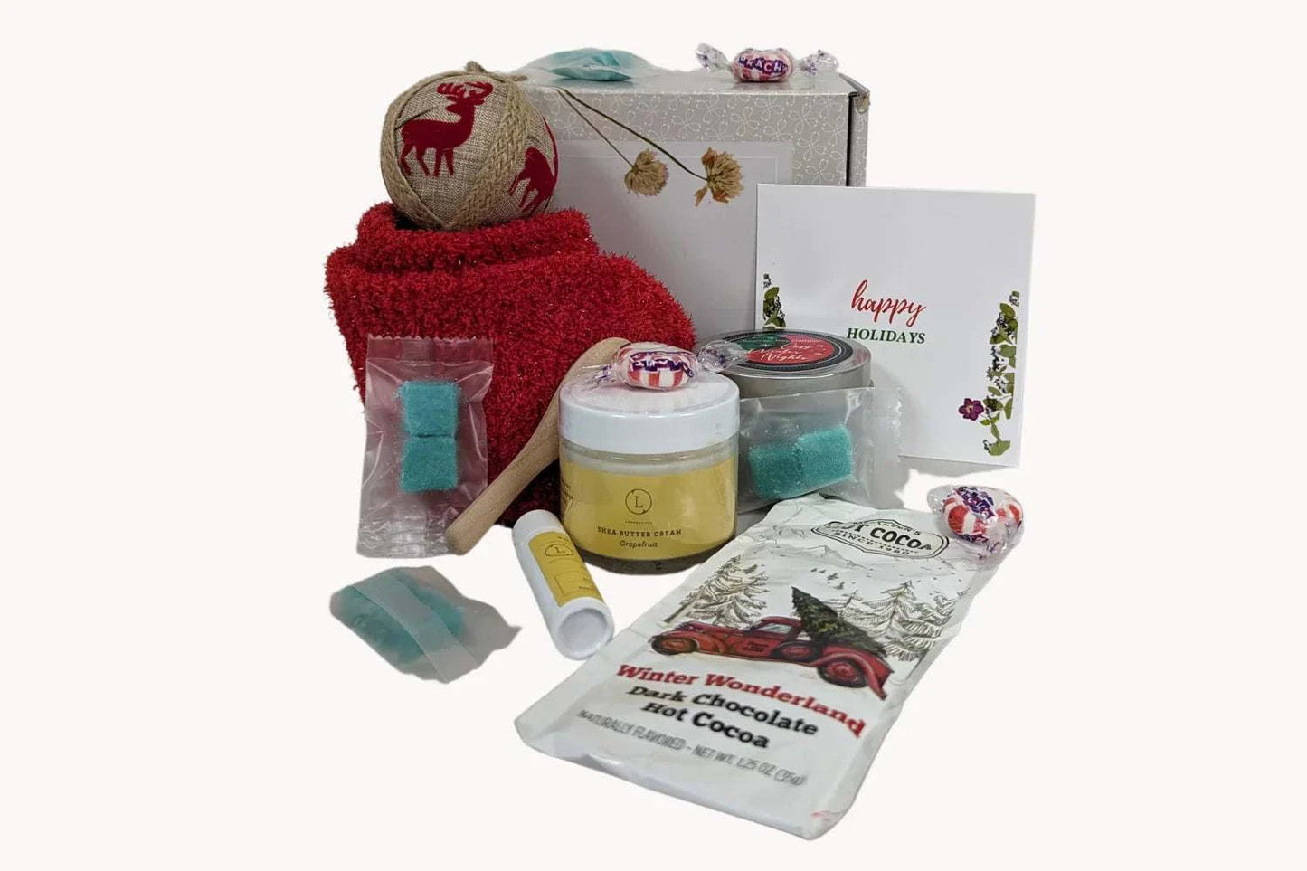 Christmas gift box for cozy nights with bath and body products, red socks, grapefruit soap, shea butter, candle, sugar scrub cubes, hot cocoa mix, and greeting card.