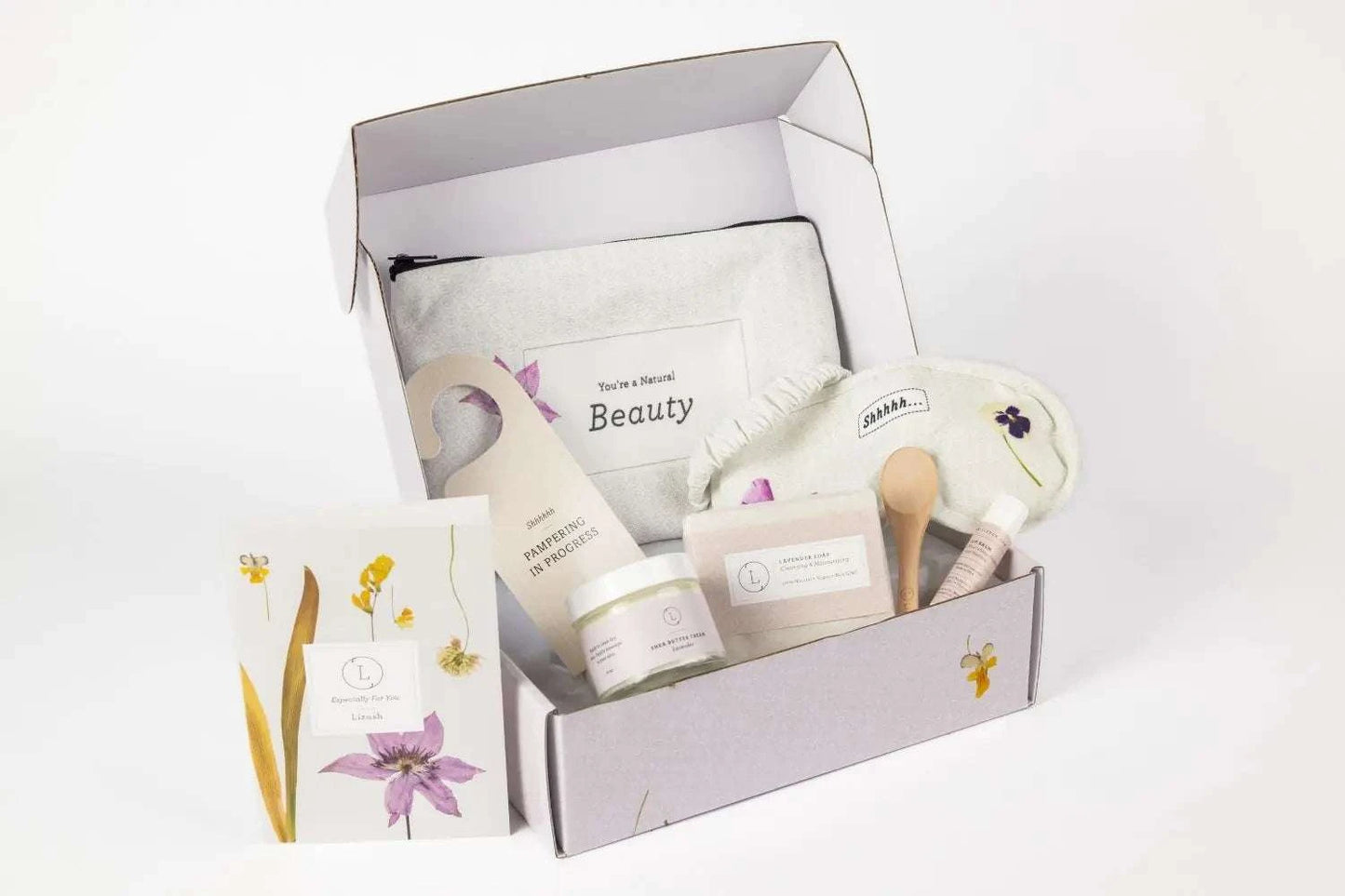Floral cosmetic bag with lavender bath and body gift set, including eye mask, soap, shea butter, and lip balm. Perfect travel toiletry kit and appreciation gift.