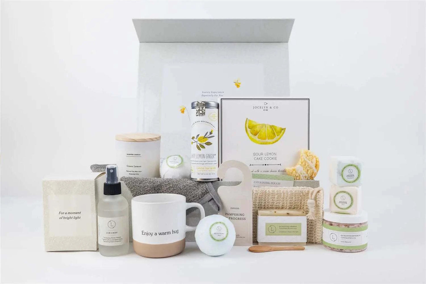 Natural care package gift basket with ceramic cup, scented candle, eucalyptus and mint bath products, tea bags, lemon cookies, and personalized options in a decorative box.