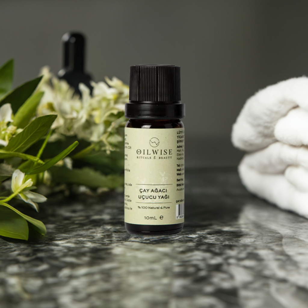 Oilwise Tea Tree Oil 10 ml bottle on marble surface with green leaves and white towel in background.