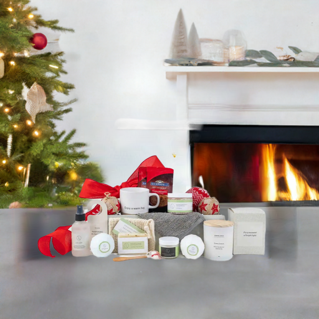 Christmas gift basket with a ceramic mug, scented candle, peppermint candies, eucalyptus bath products, foot cream, mist, hot cocoa, ornament, soap saver, and personalized options, displayed by a fireplace.