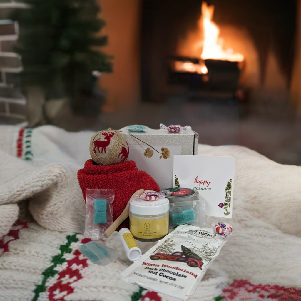 Christmas gift box for Cozy Nights with bath and body products, candle, socks, and hot cocoa mix by a fireplace.