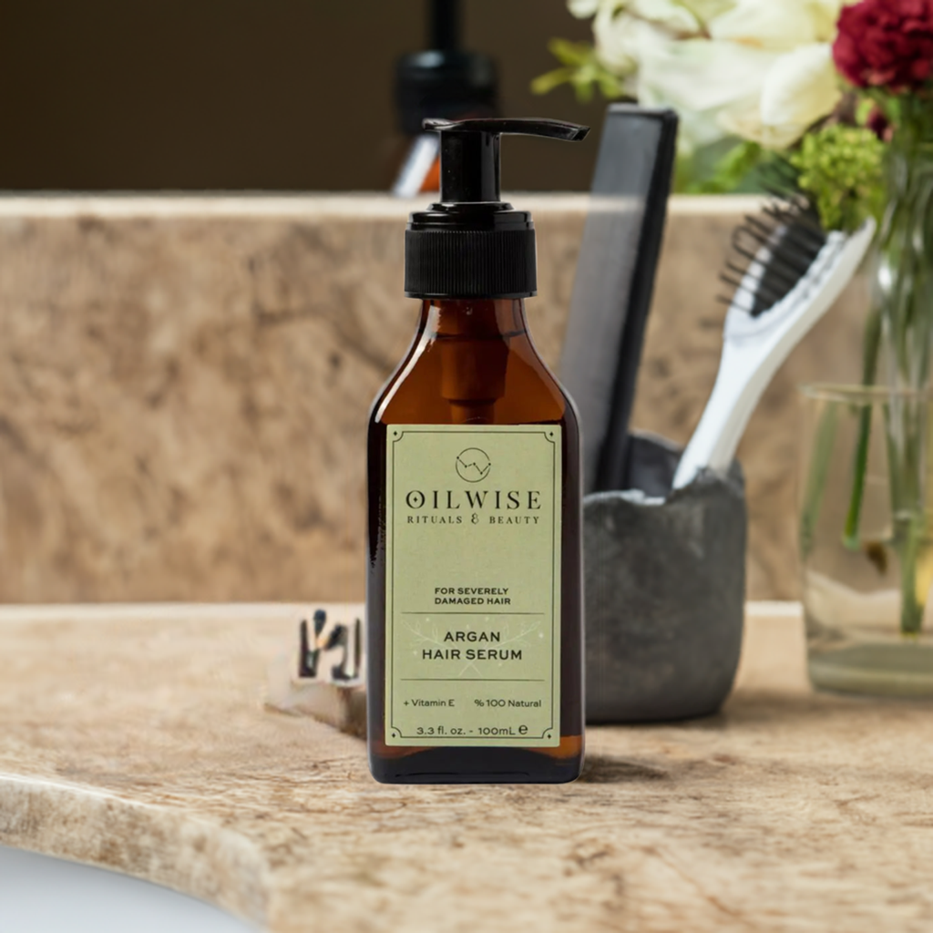 Oilwise Argan Hair Serum for Severely Damaged Hair in a pump bottle on bathroom counter with brush and flowers.