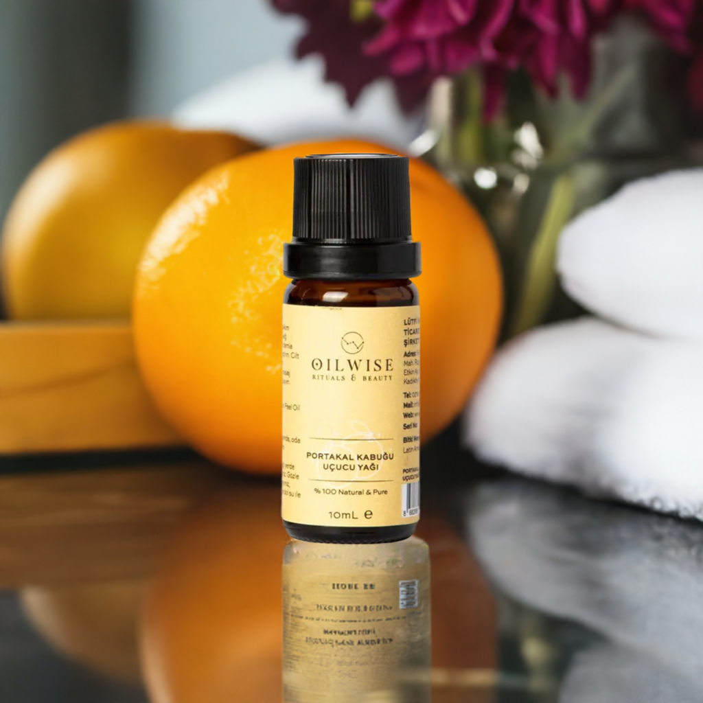 Oilwise Orange Peel Oil 10 ml bottle on a reflective surface with oranges and towels in the background.