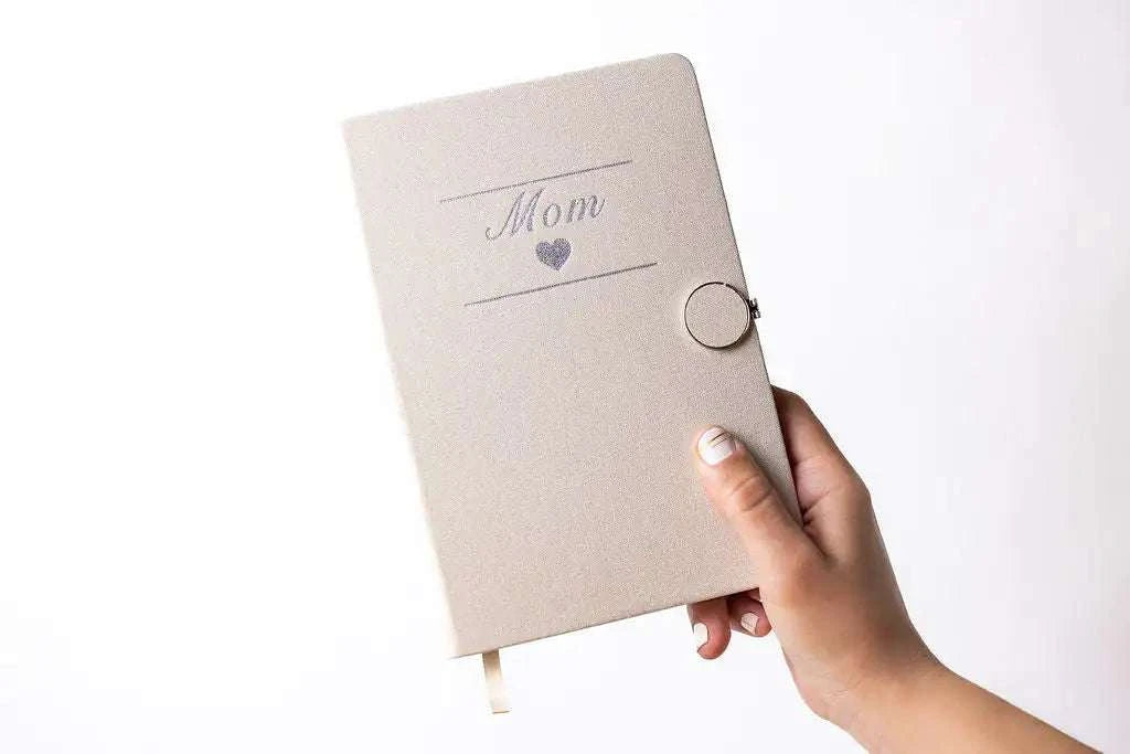 Pregnancy gift set journal with "Mom" and heart design, held in hand.