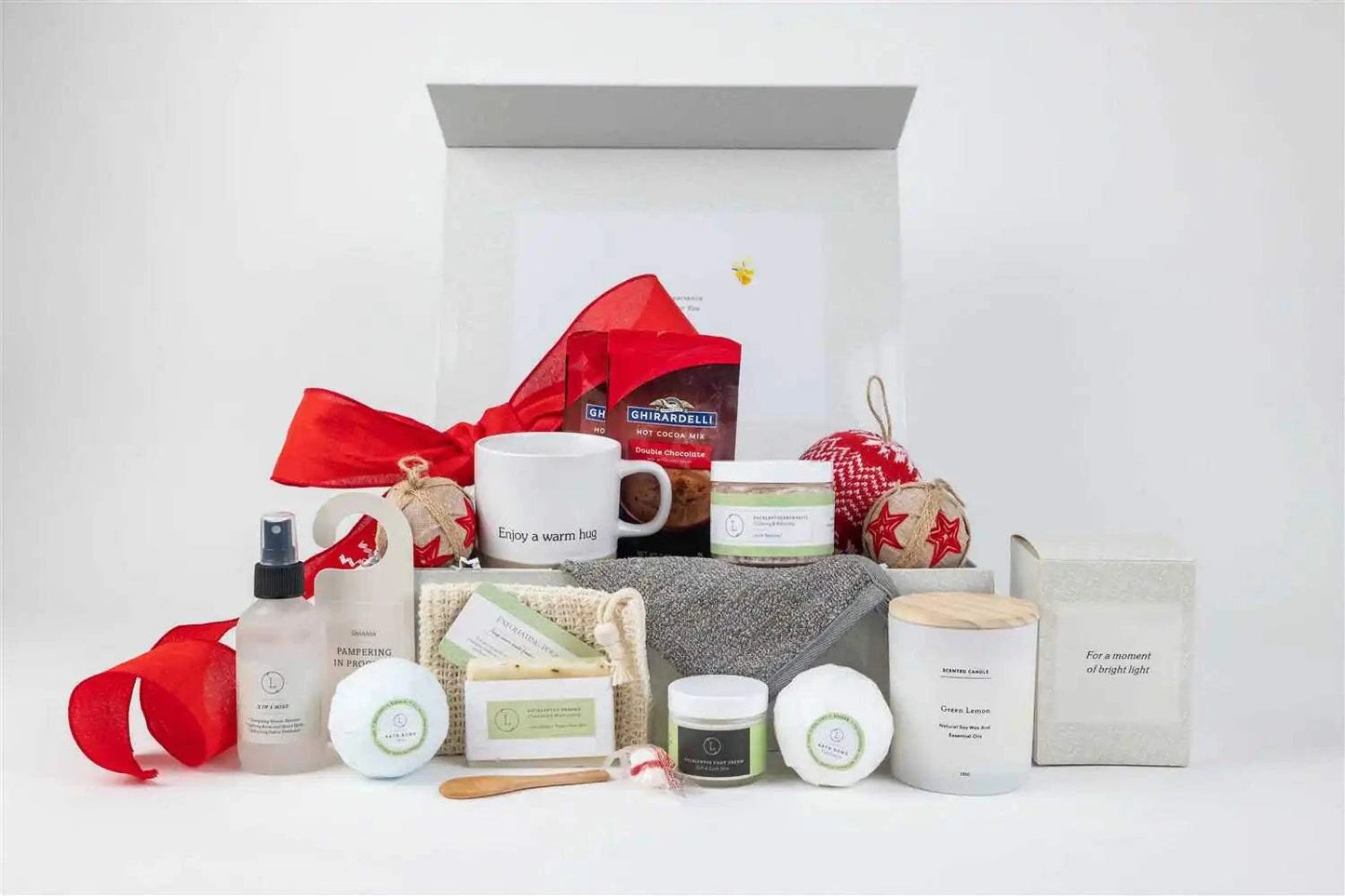 Christmas gift basket with ceramic mug, scented candle, peppermint candies, eucalyptus bath products, foot cream, mist, hot cocoa, and ornament in a decorative box.