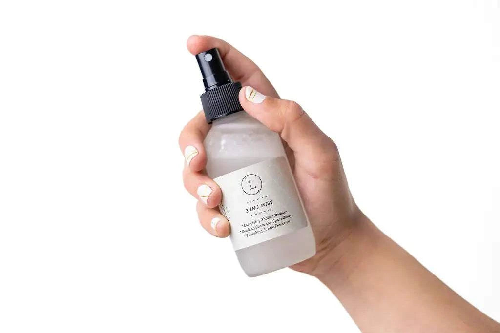 Hand holding a frosted glass bottle of shower steamer mist from the Spa Gift Box - Natural Lavender Bath & Body Relaxing Package.