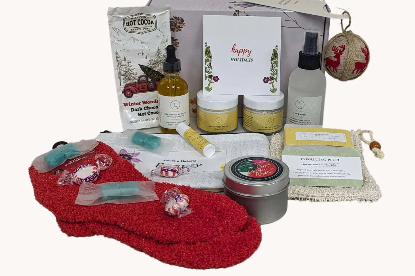 Christmas gift box with pampering spa essentials including grapefruit soap, body oil, eucalyptus mist, facial clay, cozy socks, and hot cocoa mix.