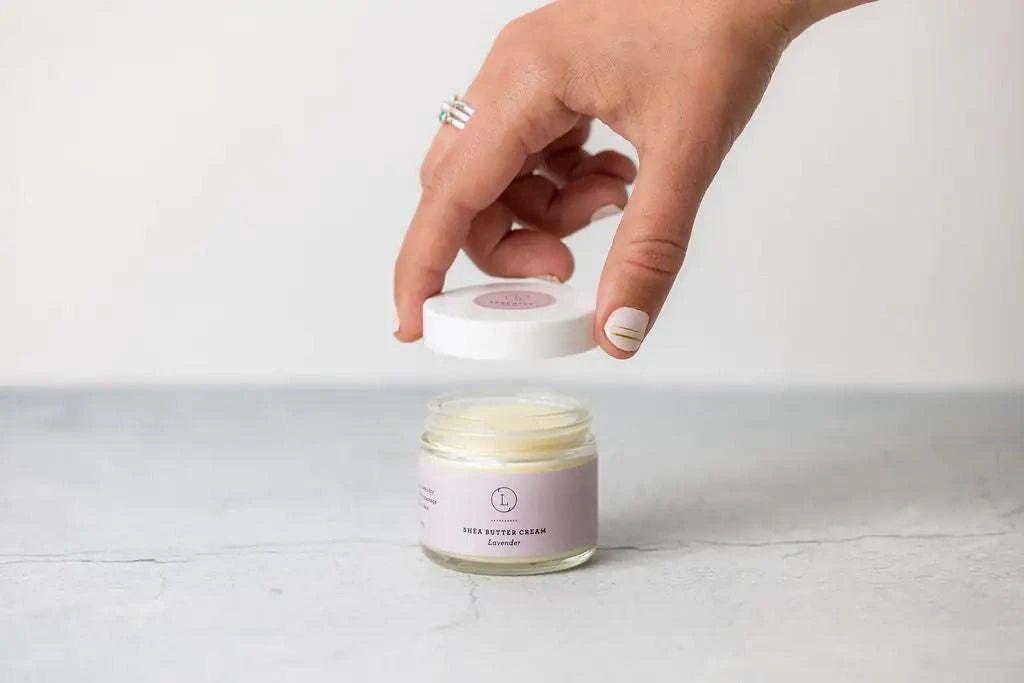 Lavender shea butter cream jar being opened, part of the Cosmetic Bag Bath and Body Gift Set, ideal travel toiletry kit for appreciation gifts.